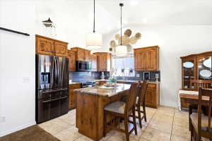 Kitchen featuring warm wood cabinetry, stainless steel appliances, a center island with bar seating, pendant lighting, and tile flooring