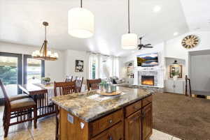 Open-concept living area featuring a kitchen island with granite countertop, a dining area with tile flooring, and a living room with a stone-surround fireplace