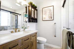 Modern primary bathroom featuring a wood-finish vanity with a white countertop and gold-tone faucet, a walk-in shower with subway tile, and a dark wood-finish wall-mounted cabinet