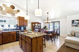 Open-concept kitchen and dining area featuring vaulted ceilings, pendant lighting, and tiled flooring