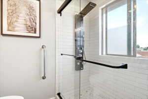 Glass-enclosed shower featuring white subway tile walls, a mosaic tile floor, and a multi-function shower panel with a rainfall shower head