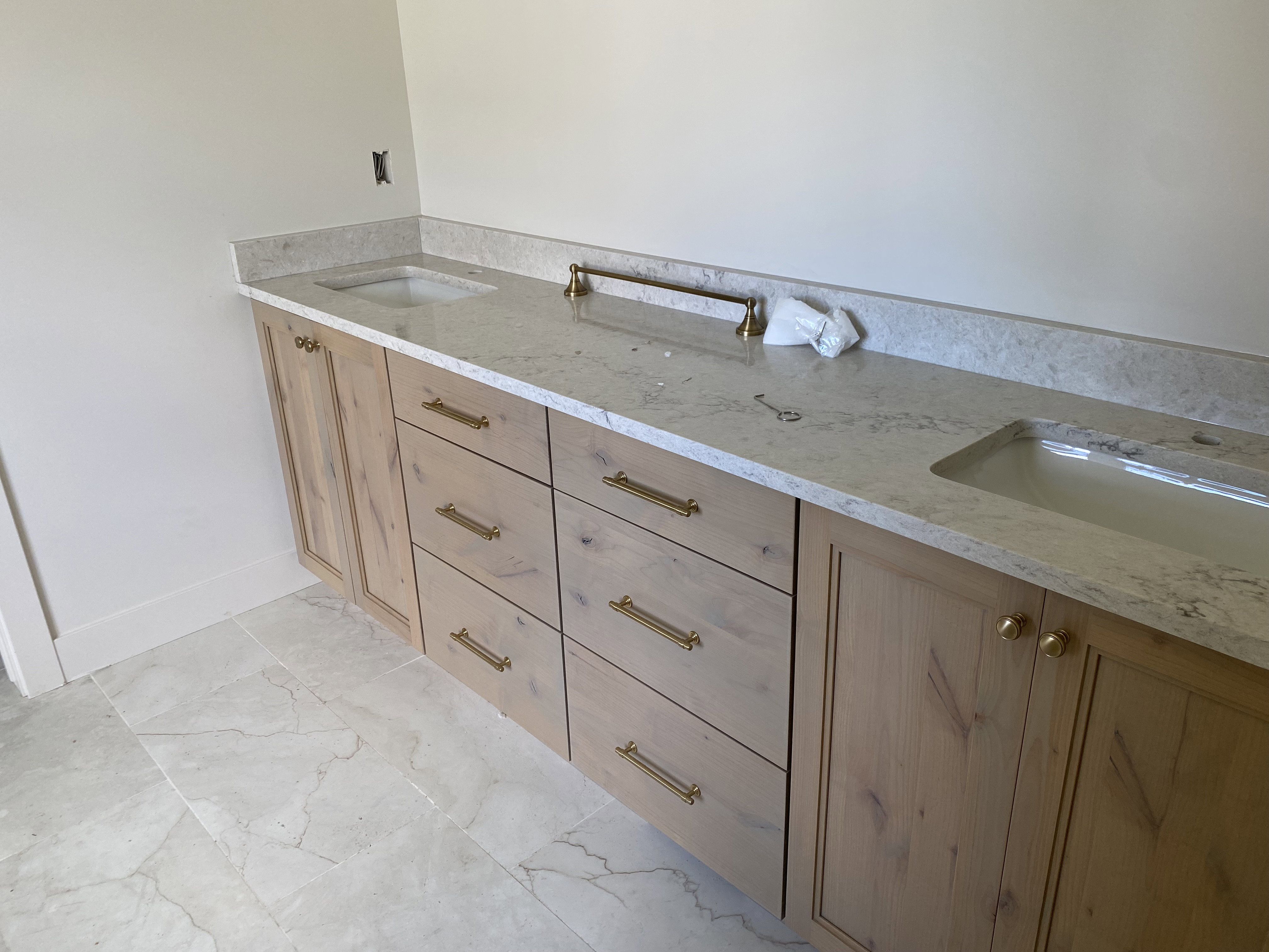 Double vanity featuring light wood cabinetry, gold-tone hardware, and light-toned stone countertops with integrated sinks