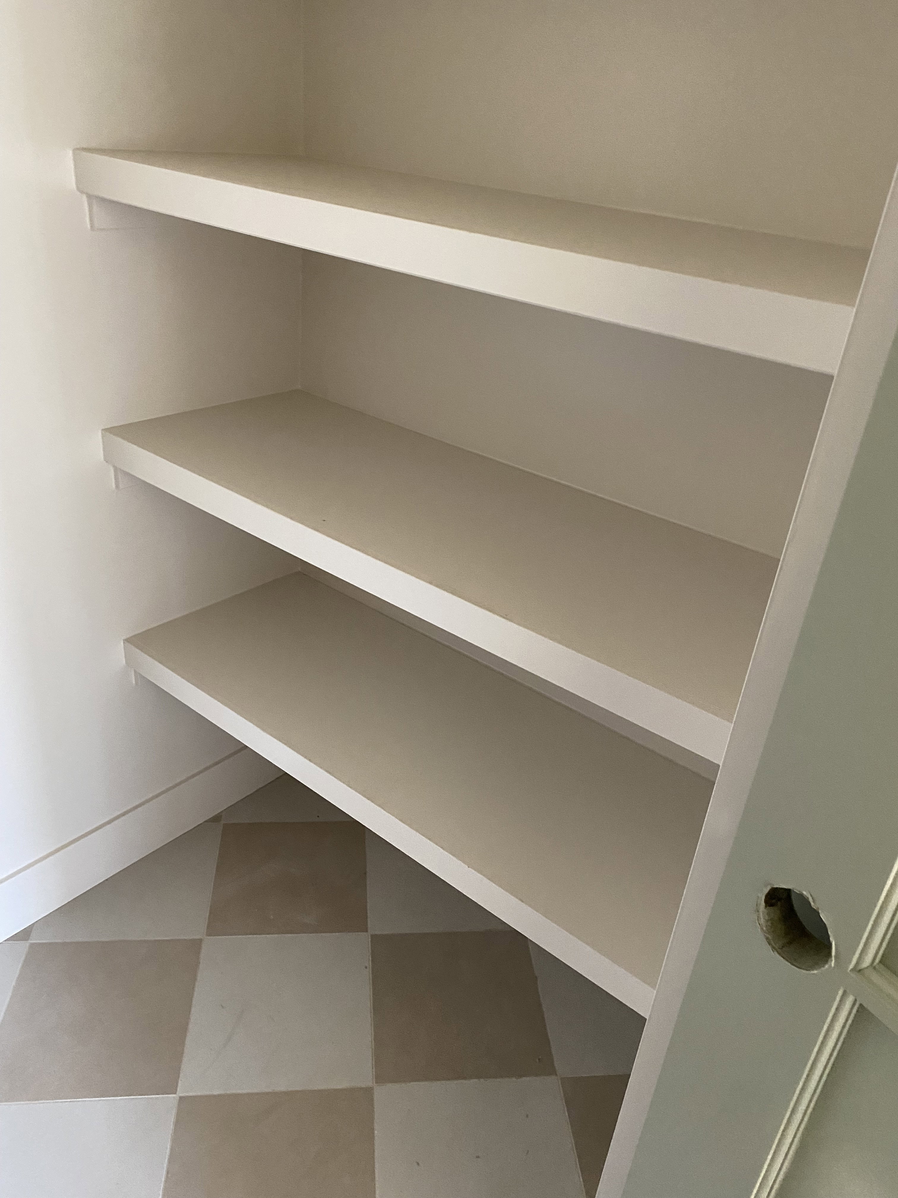 Built-in shelving unit featuring three expansive shelves, white baseboards, and two-tone checkered floor tiles