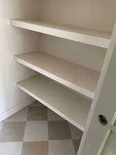 Built-in shelving unit featuring three expansive shelves, white baseboards, and two-tone checkered floor tiles
