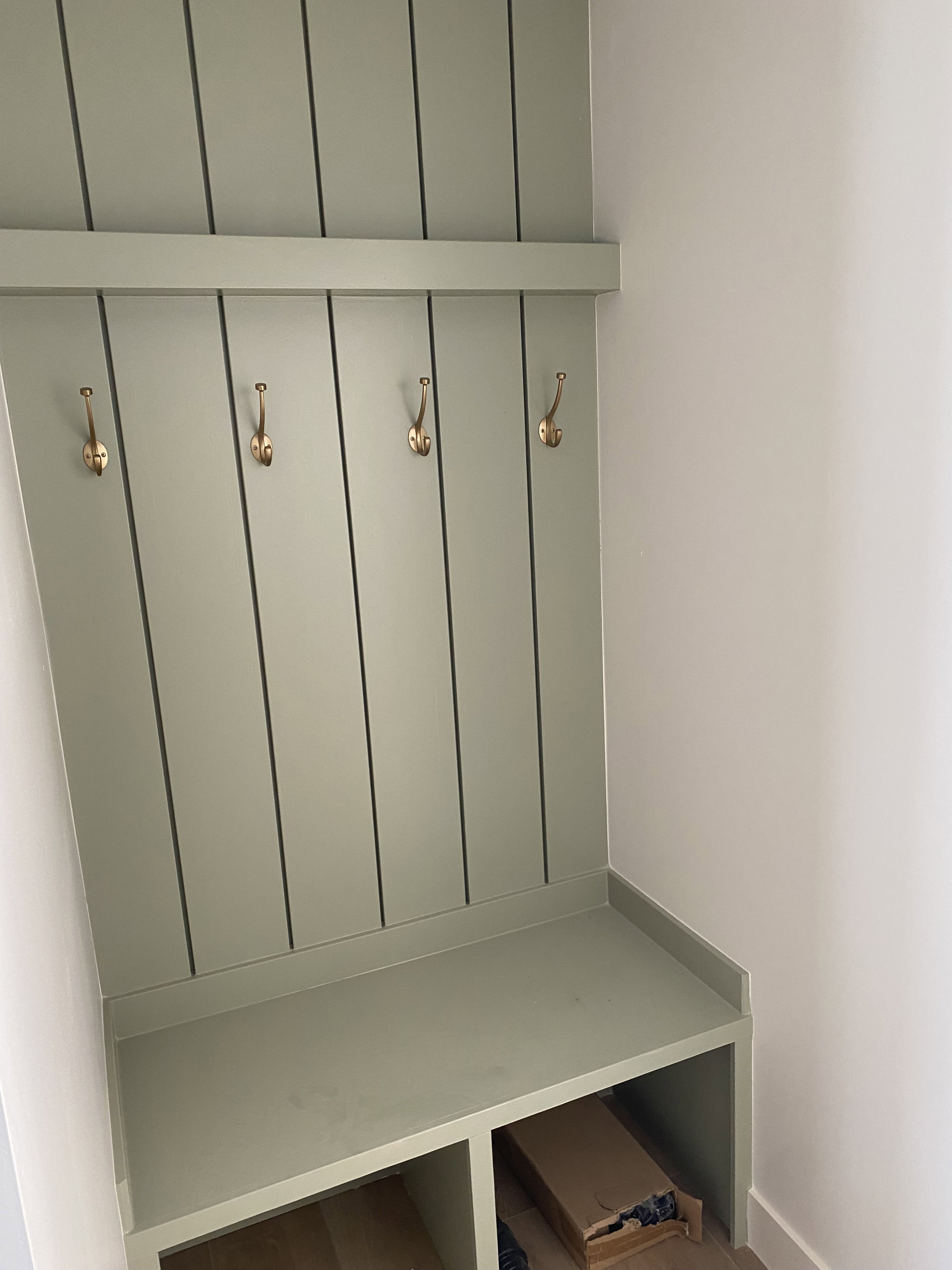 Built-in mudroom bench featuring beadboard paneling and four brass-finish hooks
