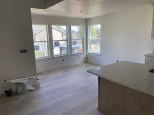 Open-concept living area featuring a light wood-finish flooring, a series of three large windows, a built-in kitchen island with a light-toned countertop, and white baseboards