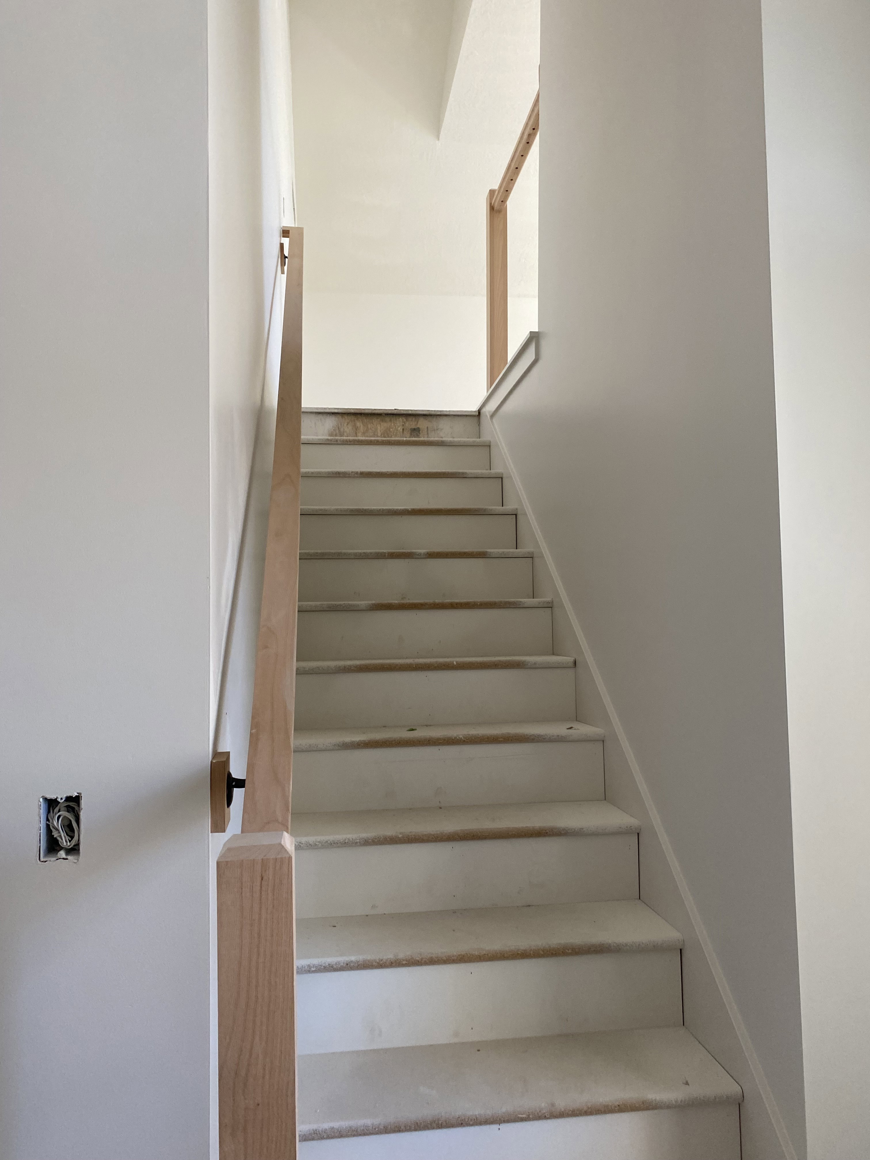 Staircase featuring light wood handrails, white risers, and light-colored treads