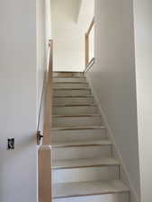 Staircase featuring light wood handrails, white risers, and light-colored treads