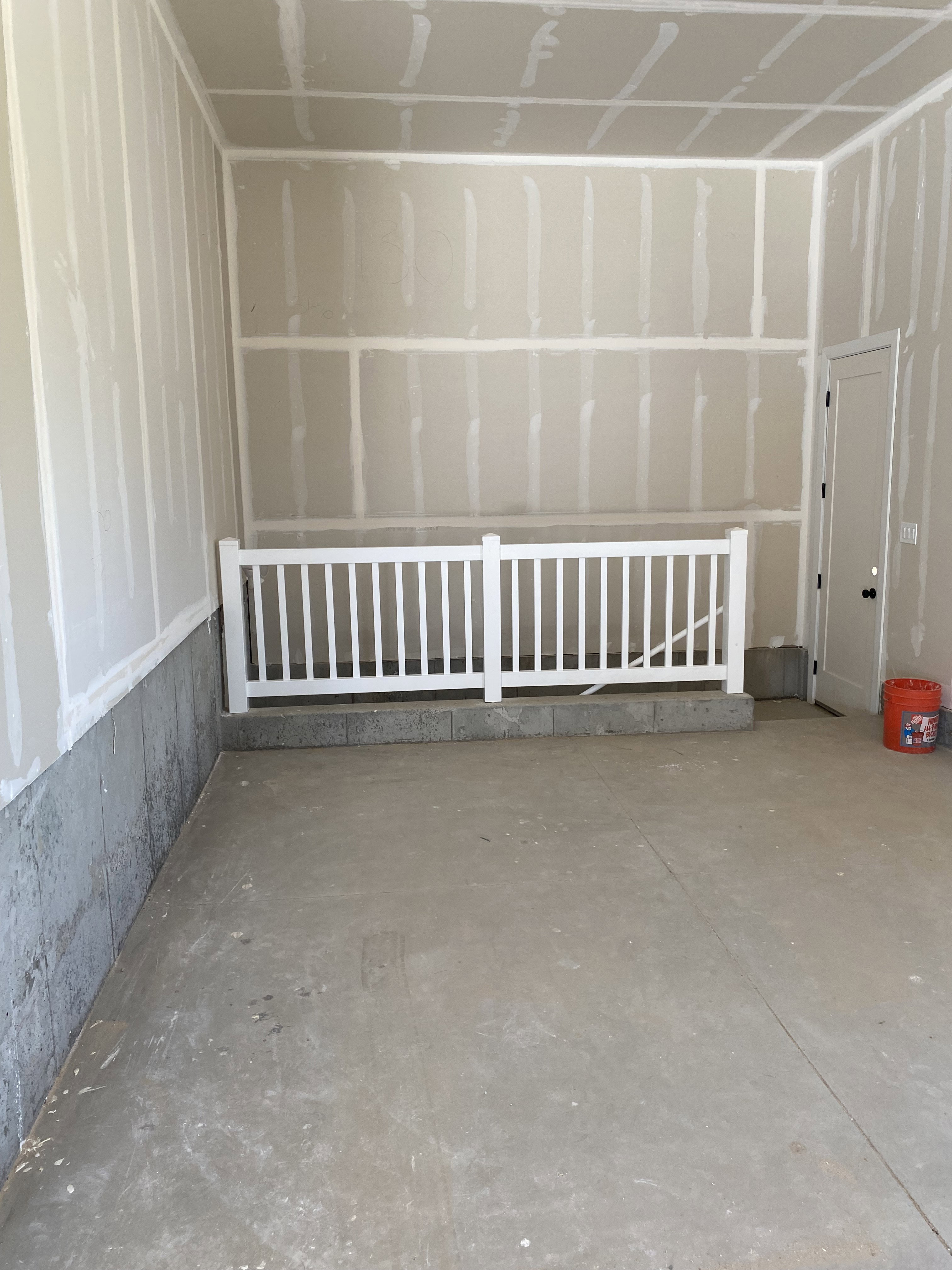 Unfinished interior space featuring a concrete floor, drywall-finished walls, and a white baluster railing