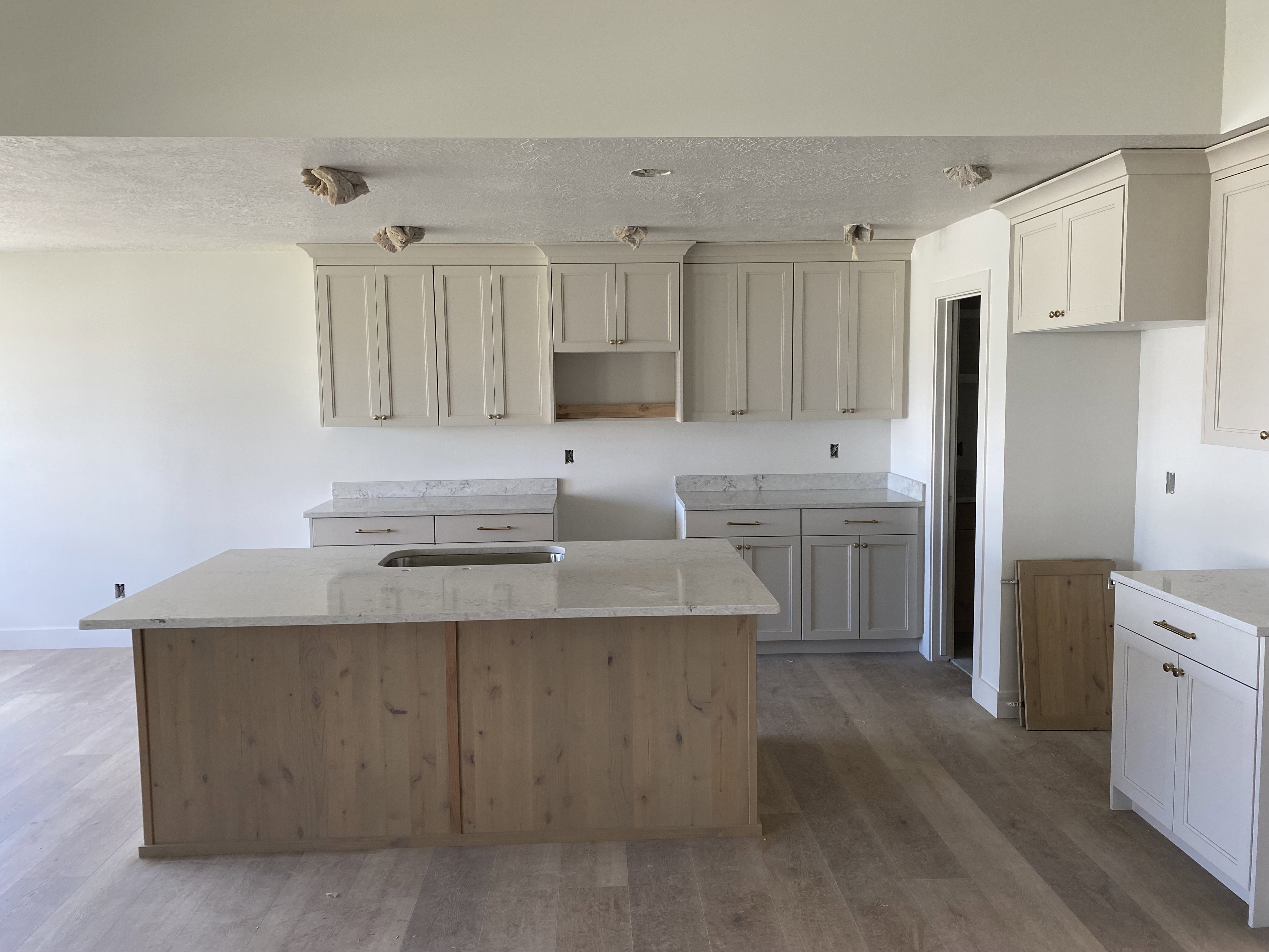 Spacious kitchen featuring a large central island with an undermount sink, light-toned wood-finish flooring, white perimeter cabinetry, and light-toned countertops throughout