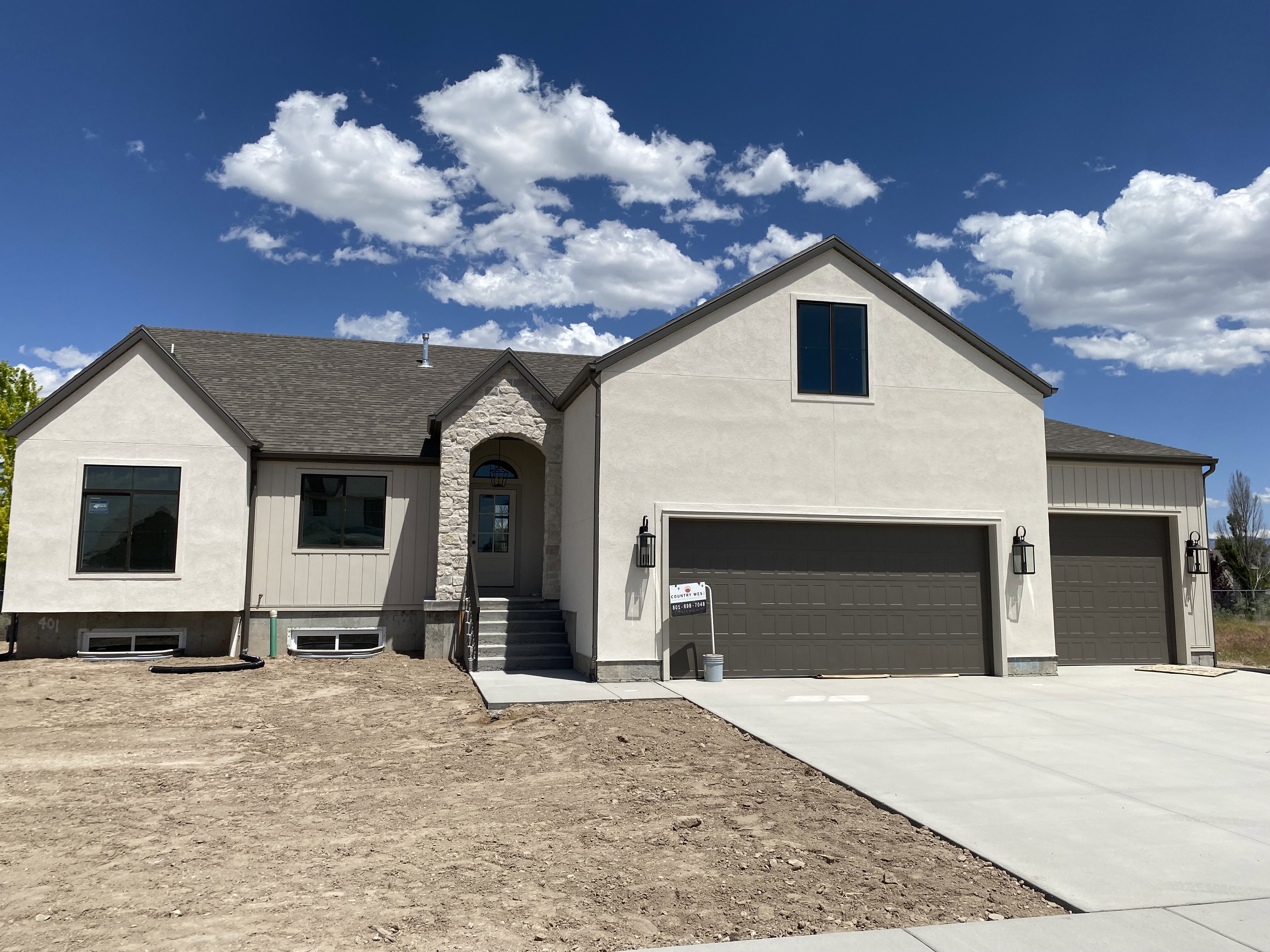 Contemporary stucco exterior with a stone archway entry, dark-framed windows, a multi-car garage, and a concrete driveway