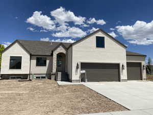 Contemporary stucco exterior with a stone archway entry, dark-framed windows, a multi-car garage, and a concrete driveway
