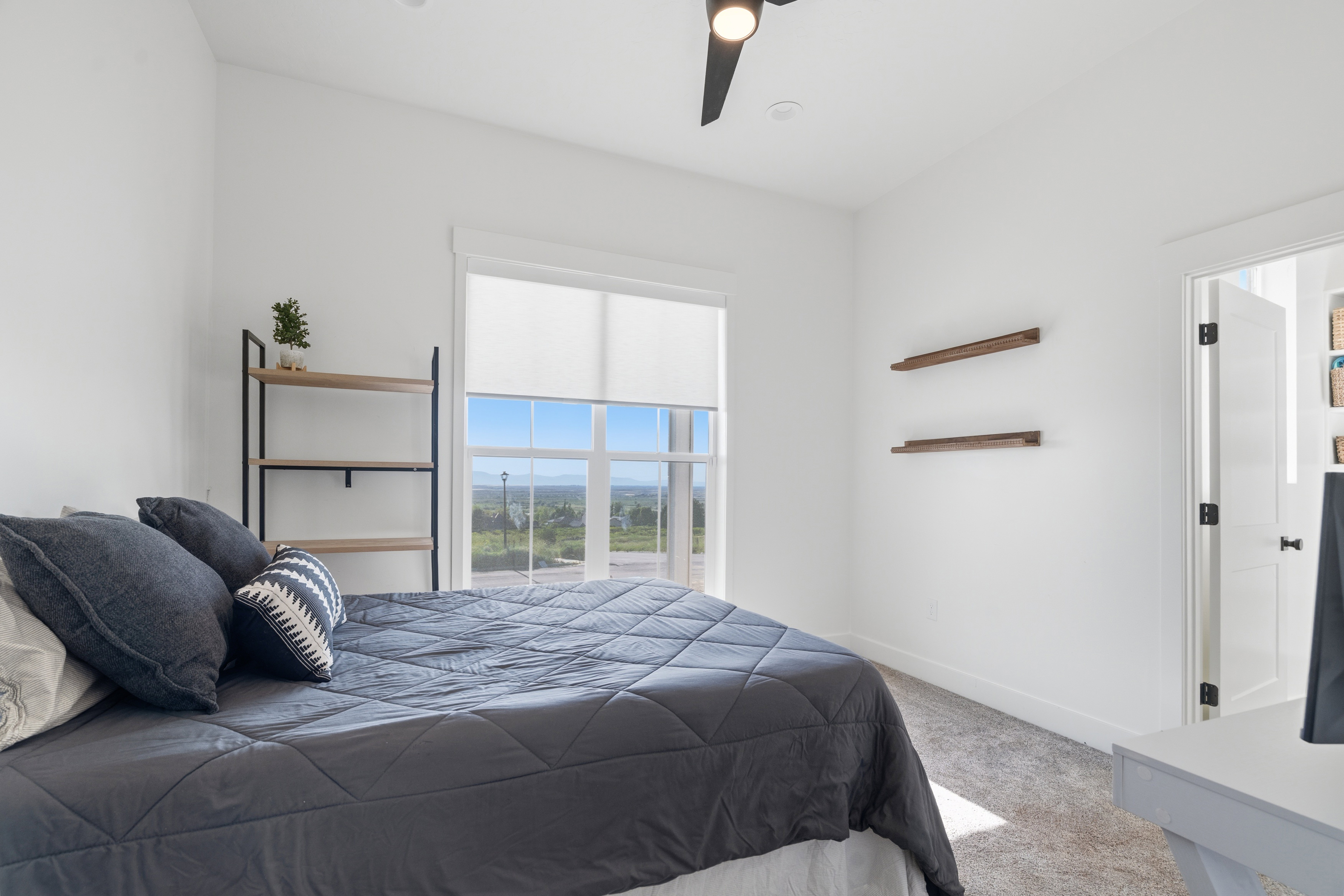 Bright interior space featuring a large window with roller shades, white walls, and light-toned carpeting