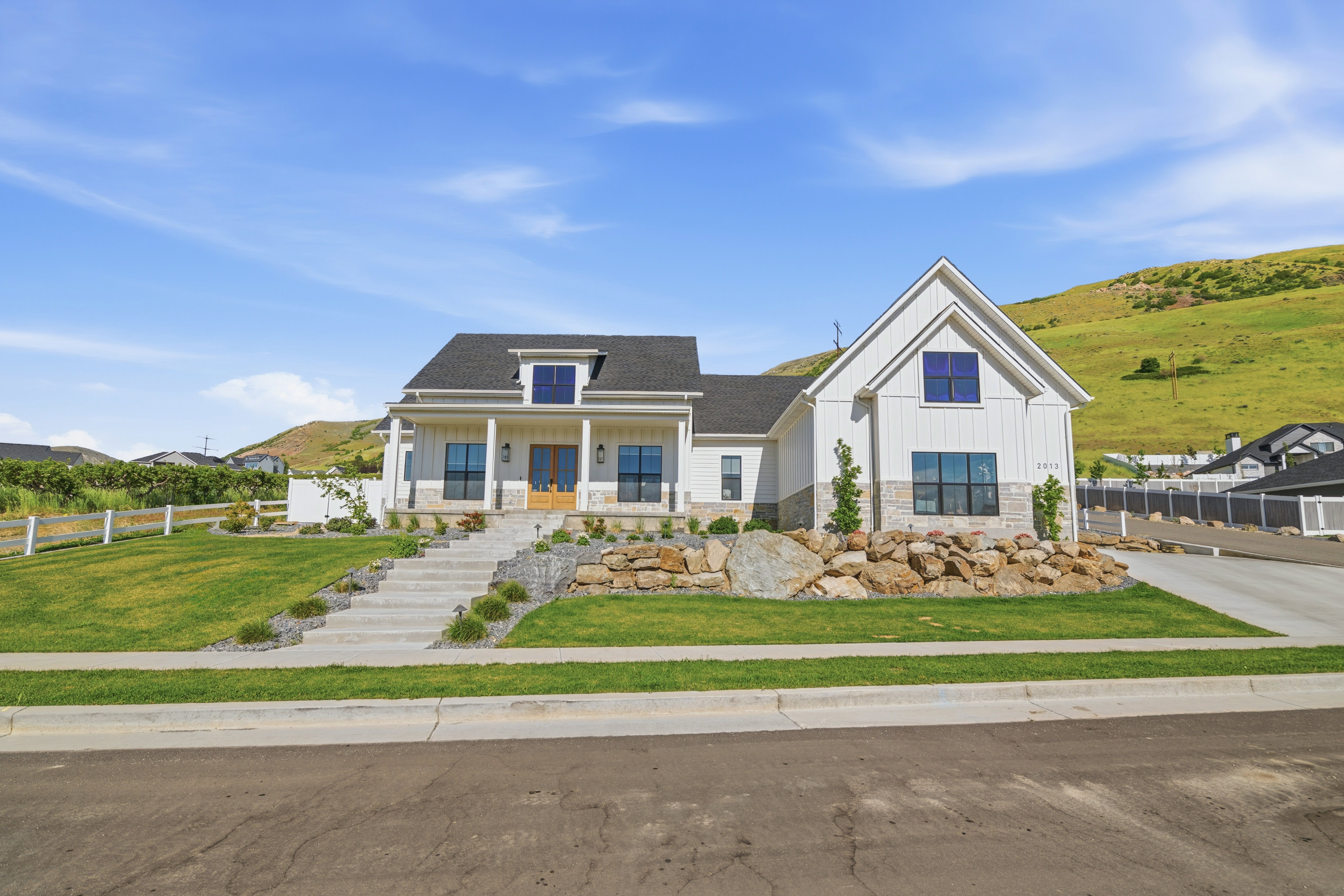 Modern farmhouse exterior with white board-and-batten siding, dark shingle roof, stone accents, and a covered front porch with columns