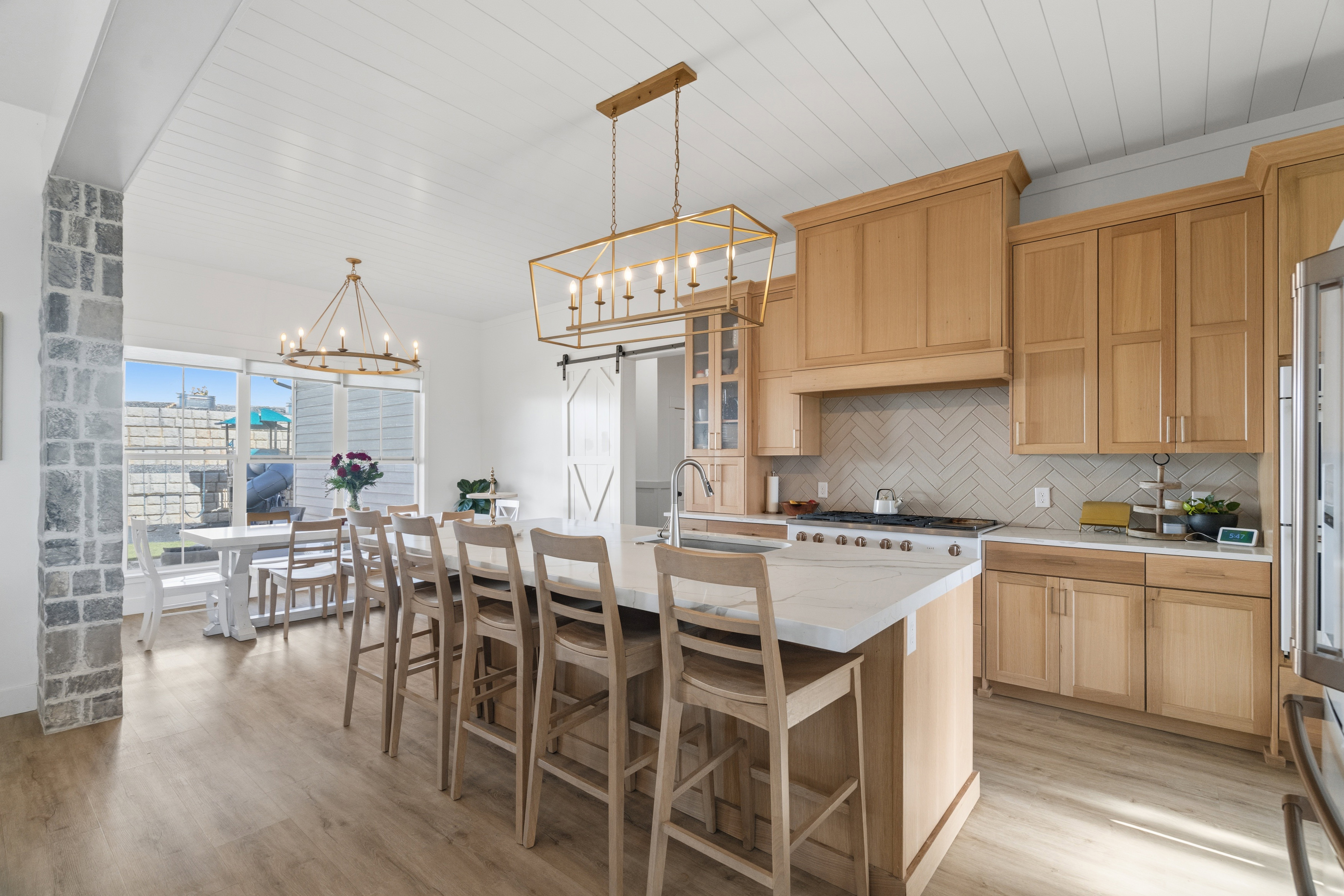 Gourmet kitchen and dining area featuring light wood cabinetry, a large center island with seating, white countertops, and a herringbone tile backsplash