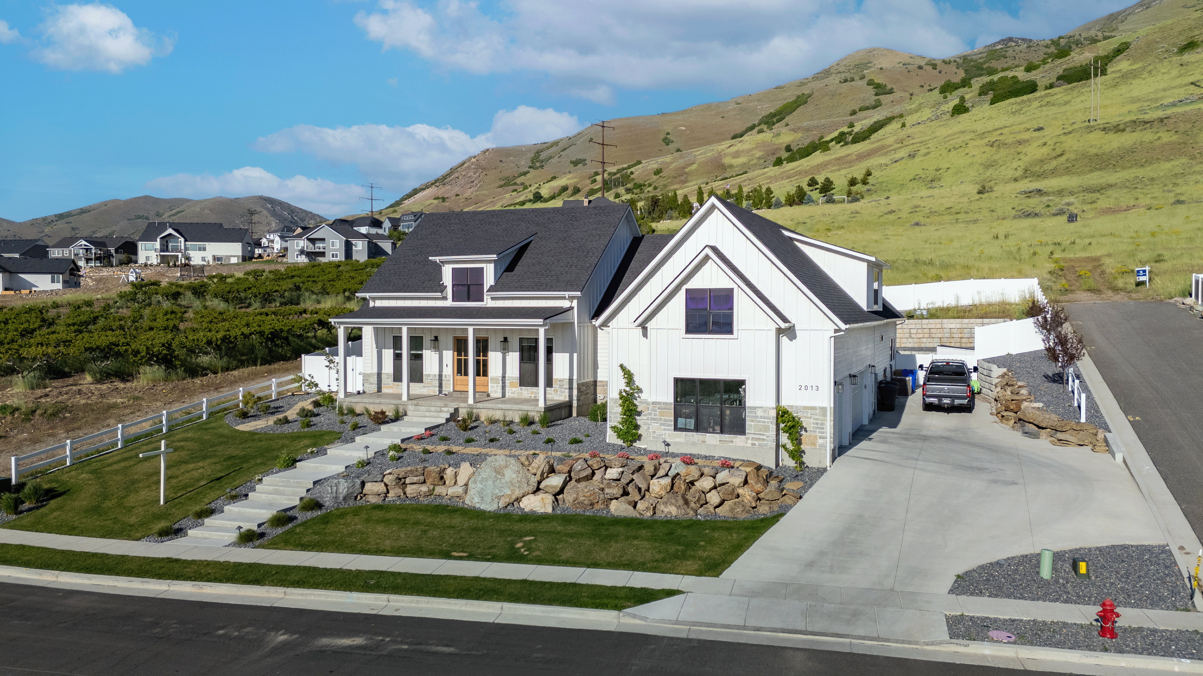 Modern farmhouse-style residence featuring white vertical siding, a dark shingle roof, and stone accents