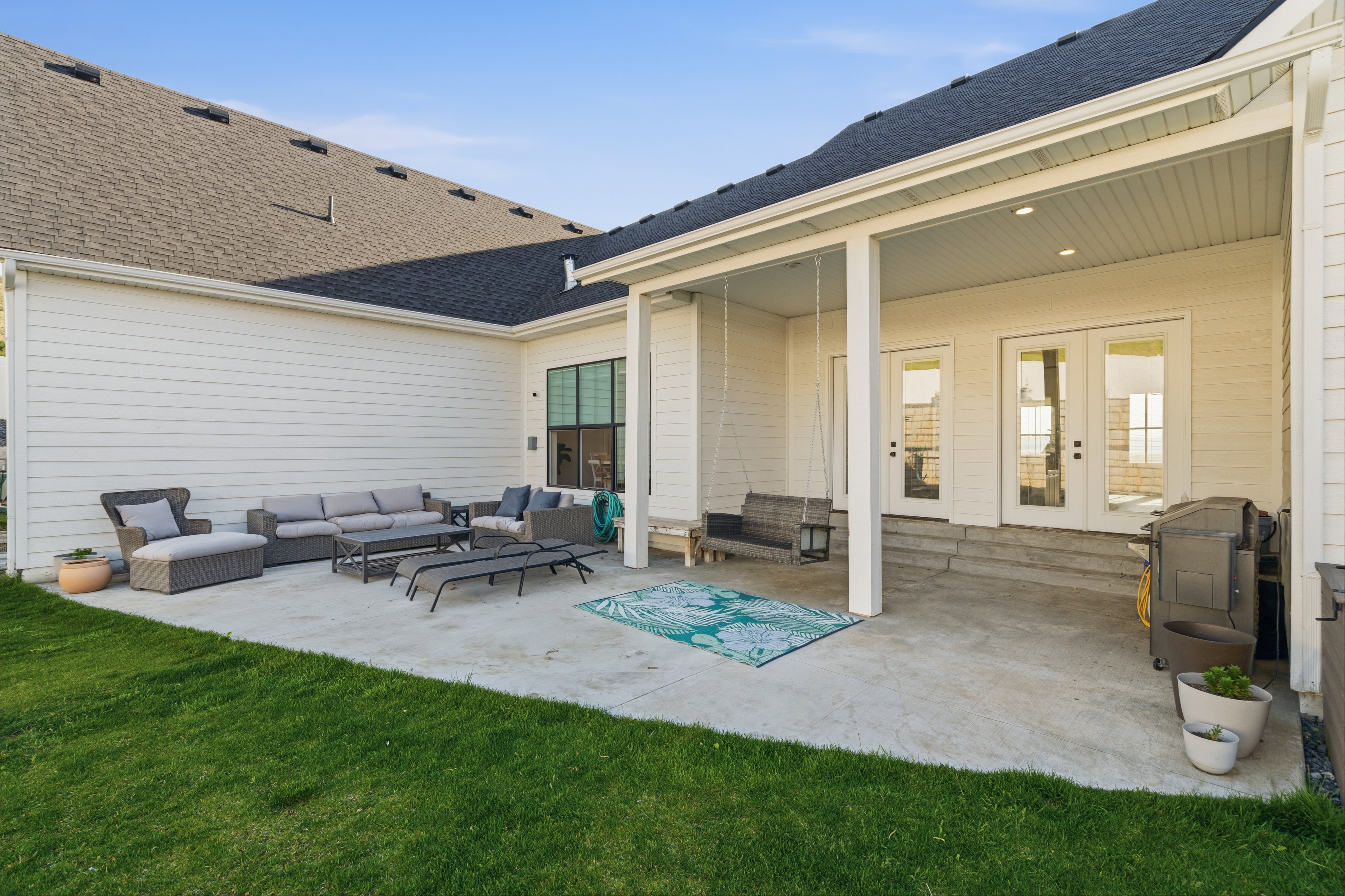 Spacious concrete patio with a covered porch, white siding, multiple French doors, and a dark shingle roof