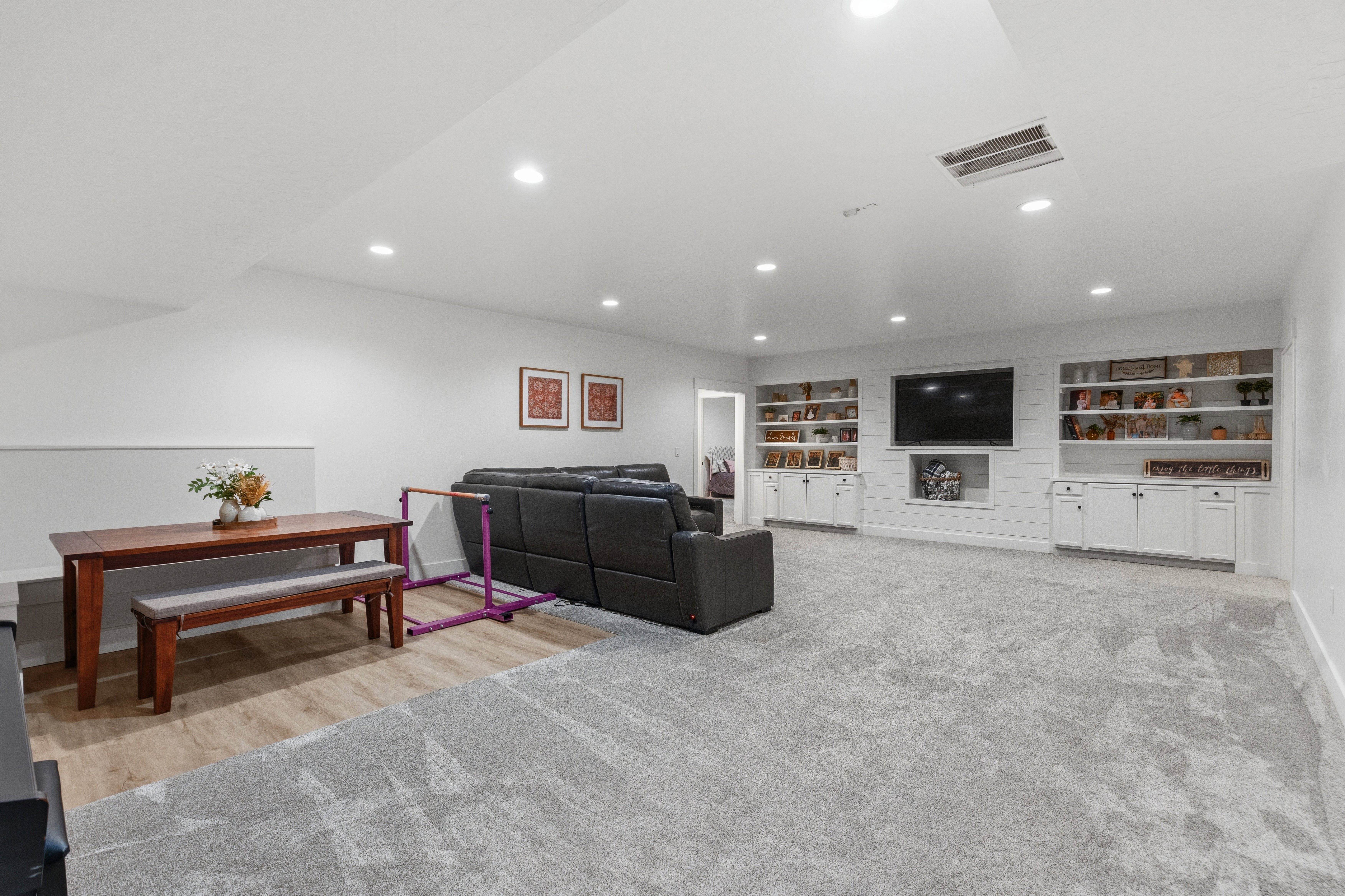 Spacious multi-zone interior featuring recessed lighting, a built-in entertainment center with open shelving and lower cabinetry, wood-finish flooring, and soft grey carpeting