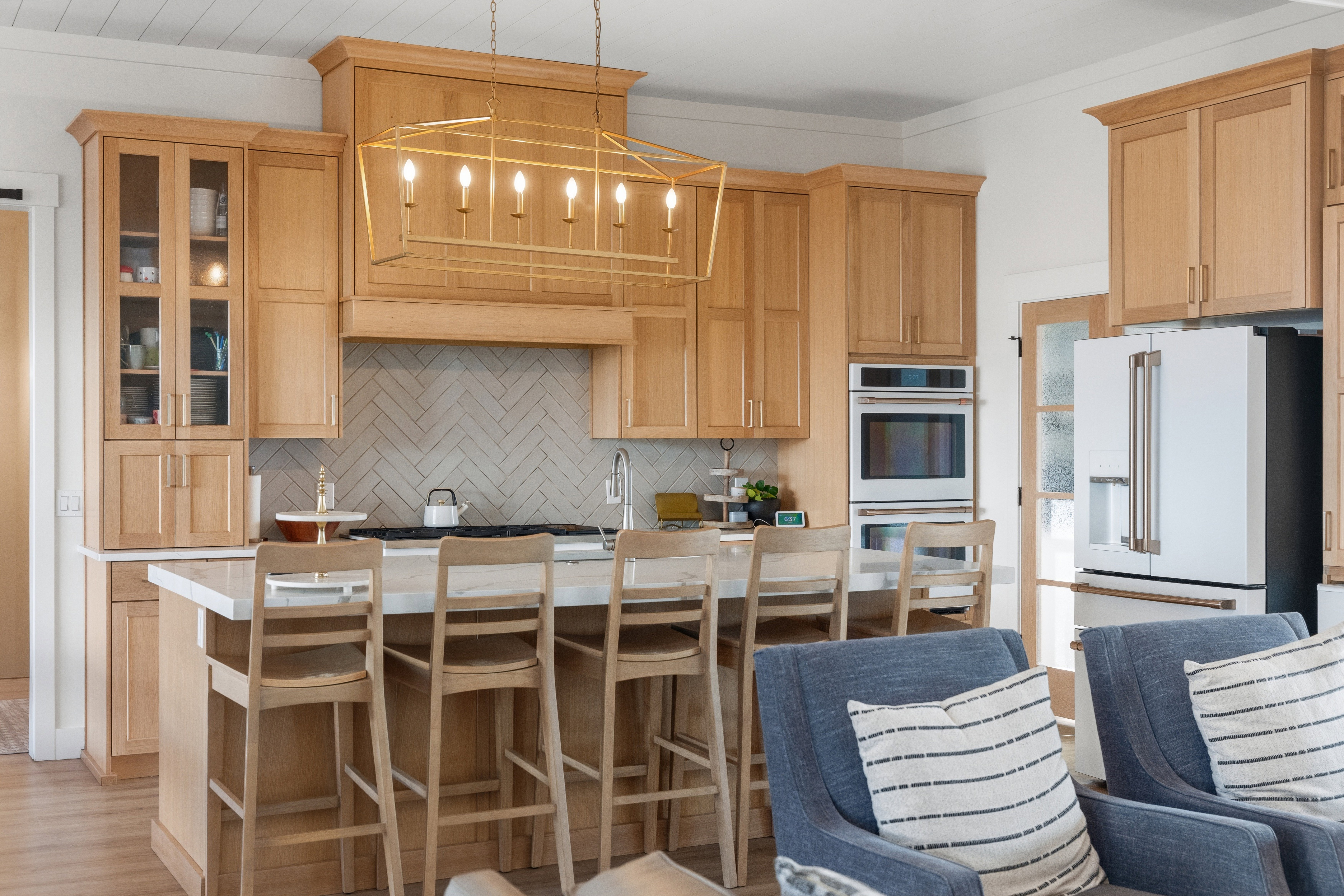 Gourmet kitchen featuring a central island with seating, natural wood-finish cabinetry, integrated stainless steel appliances, a herringbone tile backsplash, and a contemporary chandelier