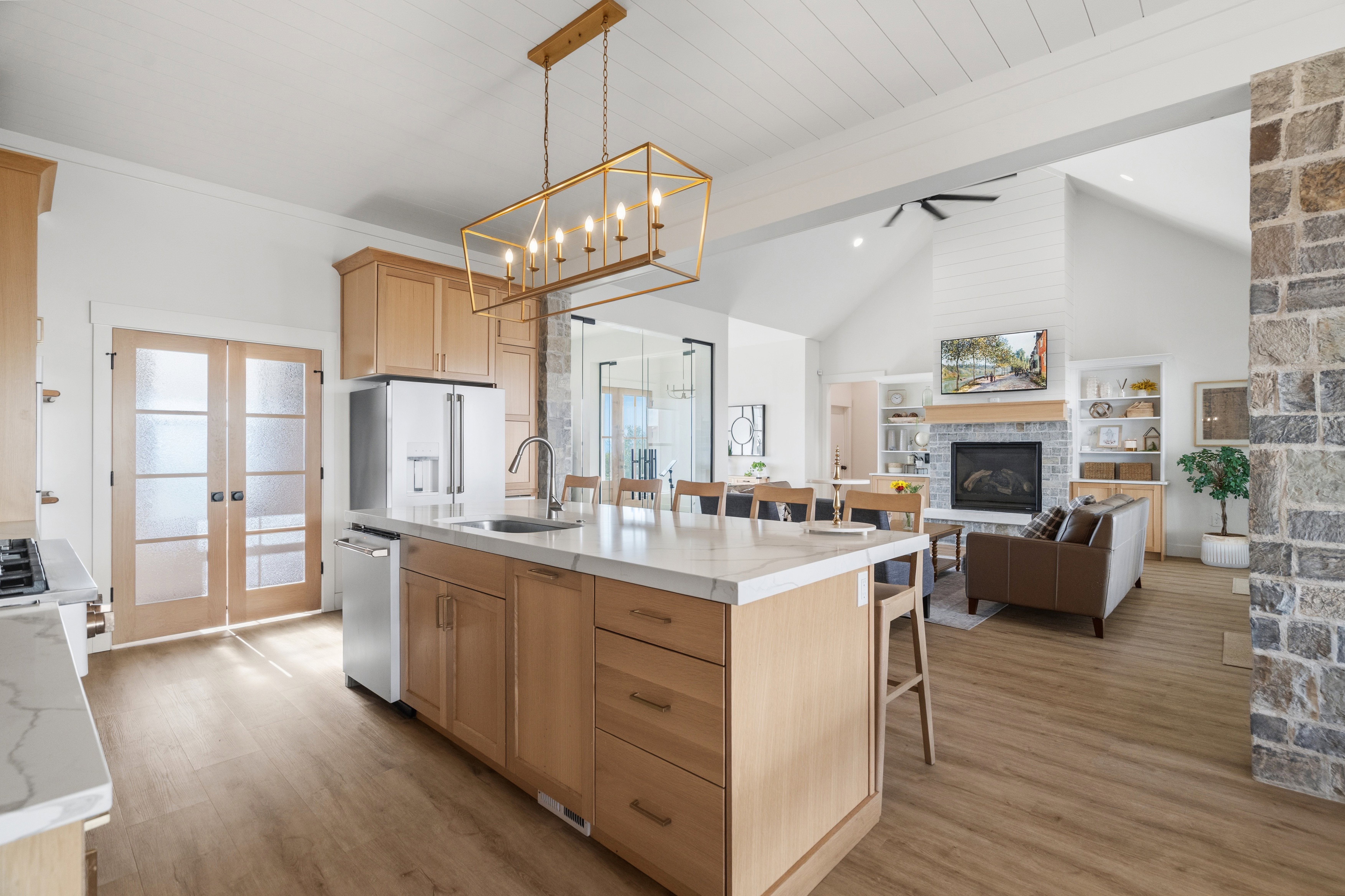 Open-concept kitchen and living area featuring a large center island with seating, natural wood cabinetry, wood-finish flooring, and a stone accent wall