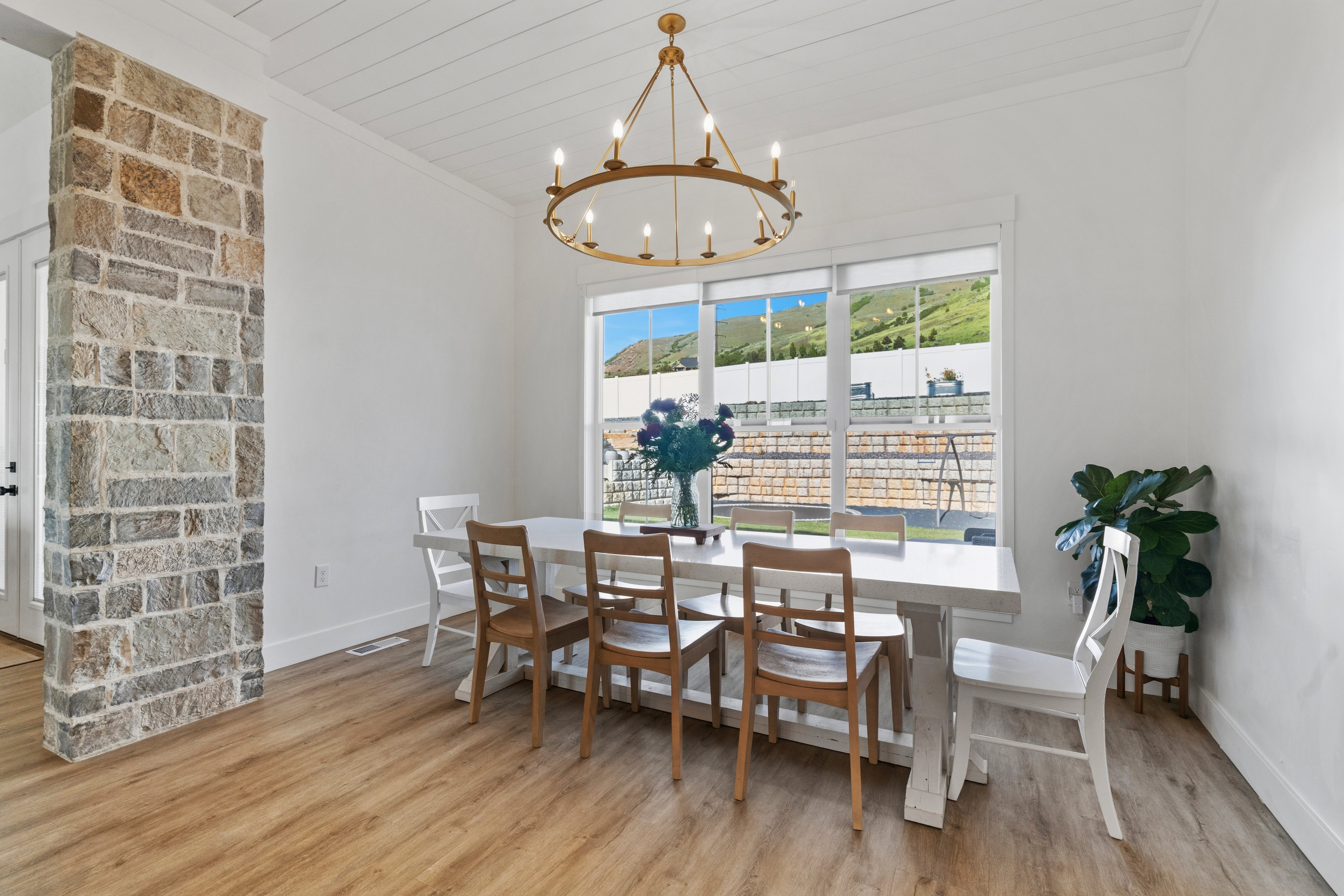 Dining area featuring a gold-finish chandelier, wood-finish flooring, and a stone-clad architectural column