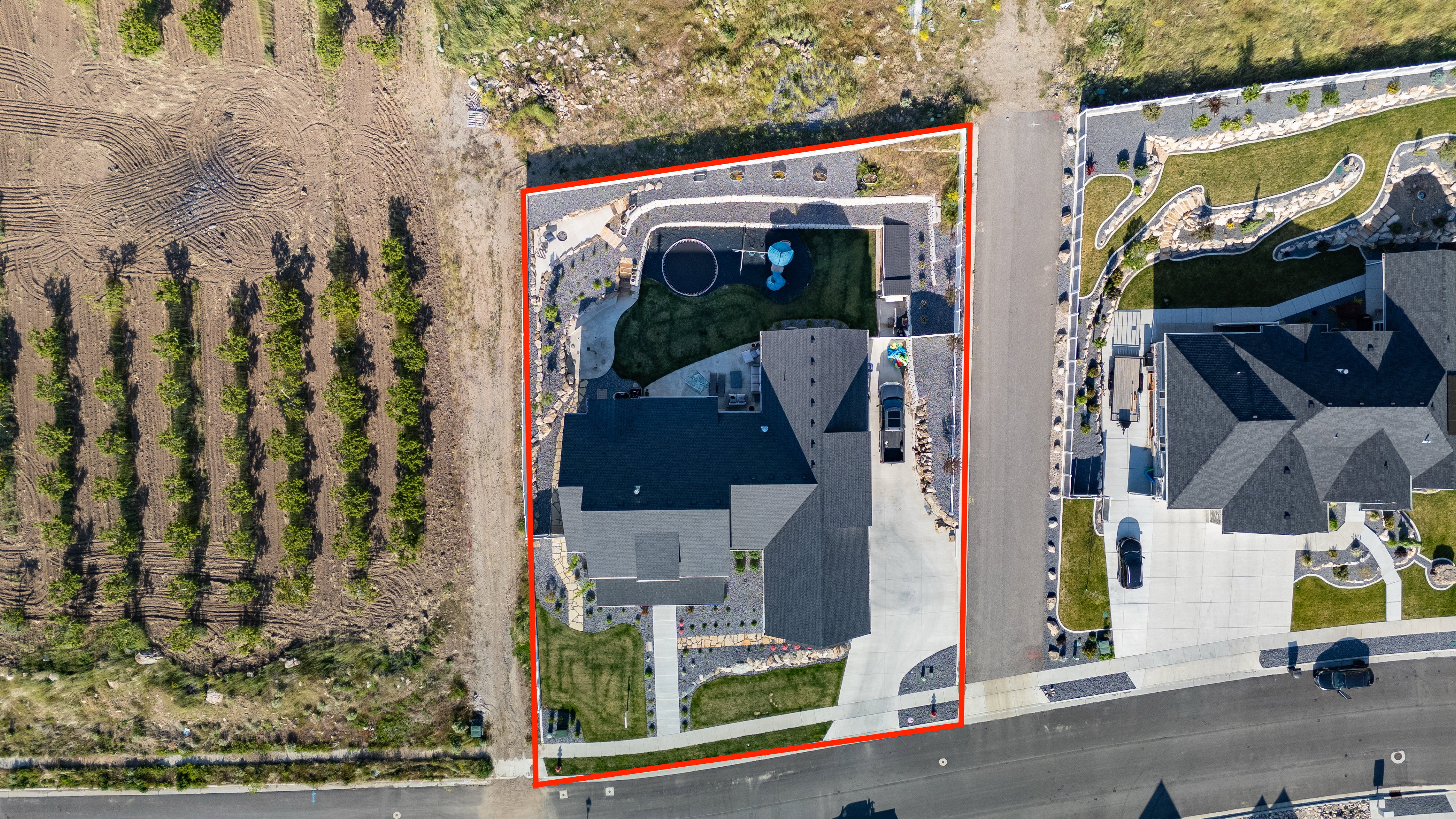 Aerial view showcasing a property with a dark shingle roof, concrete driveways, and landscaped grounds