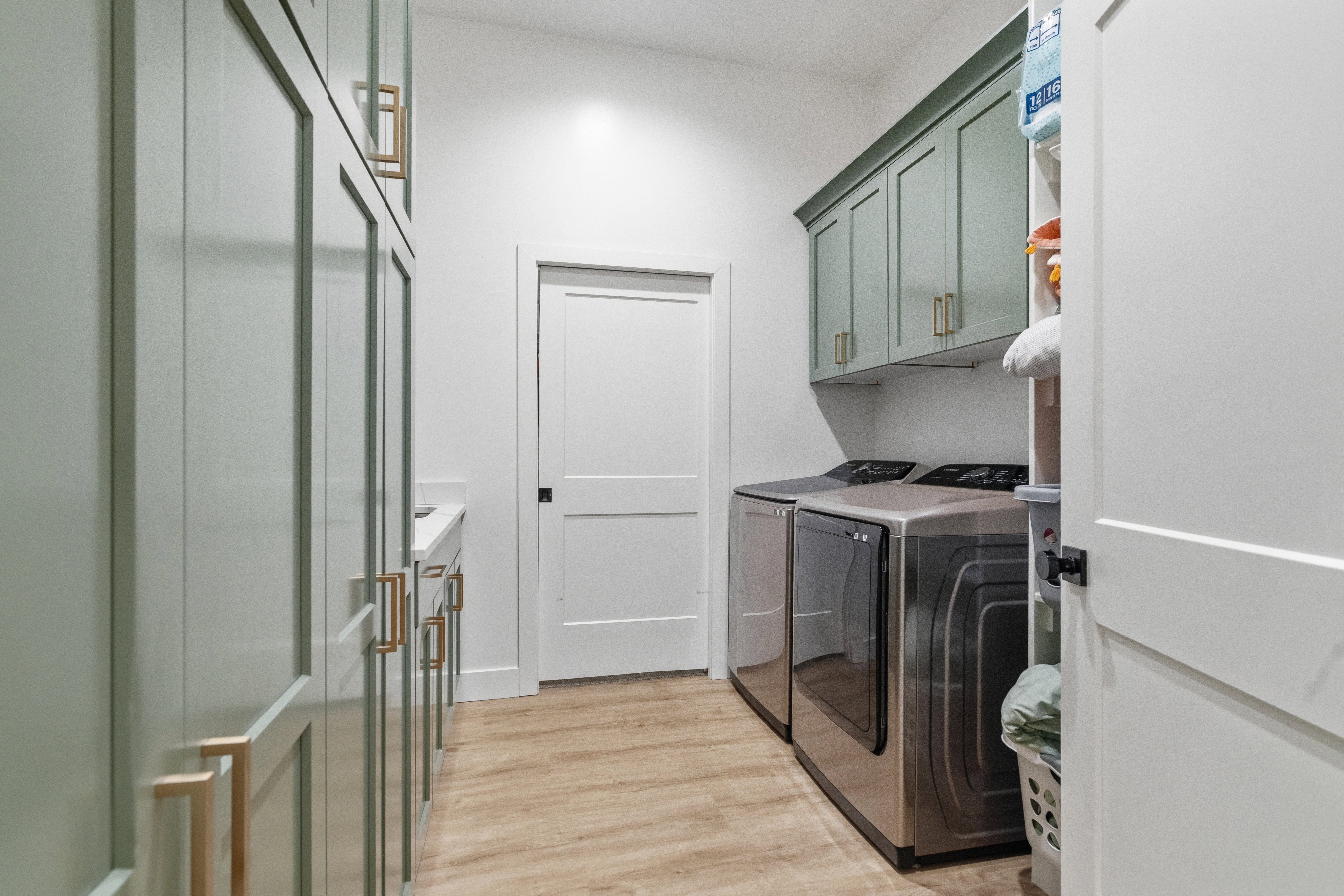 Laundry room featuring light green cabinetry with gold-toned hardware, wood-finish flooring, and white walls