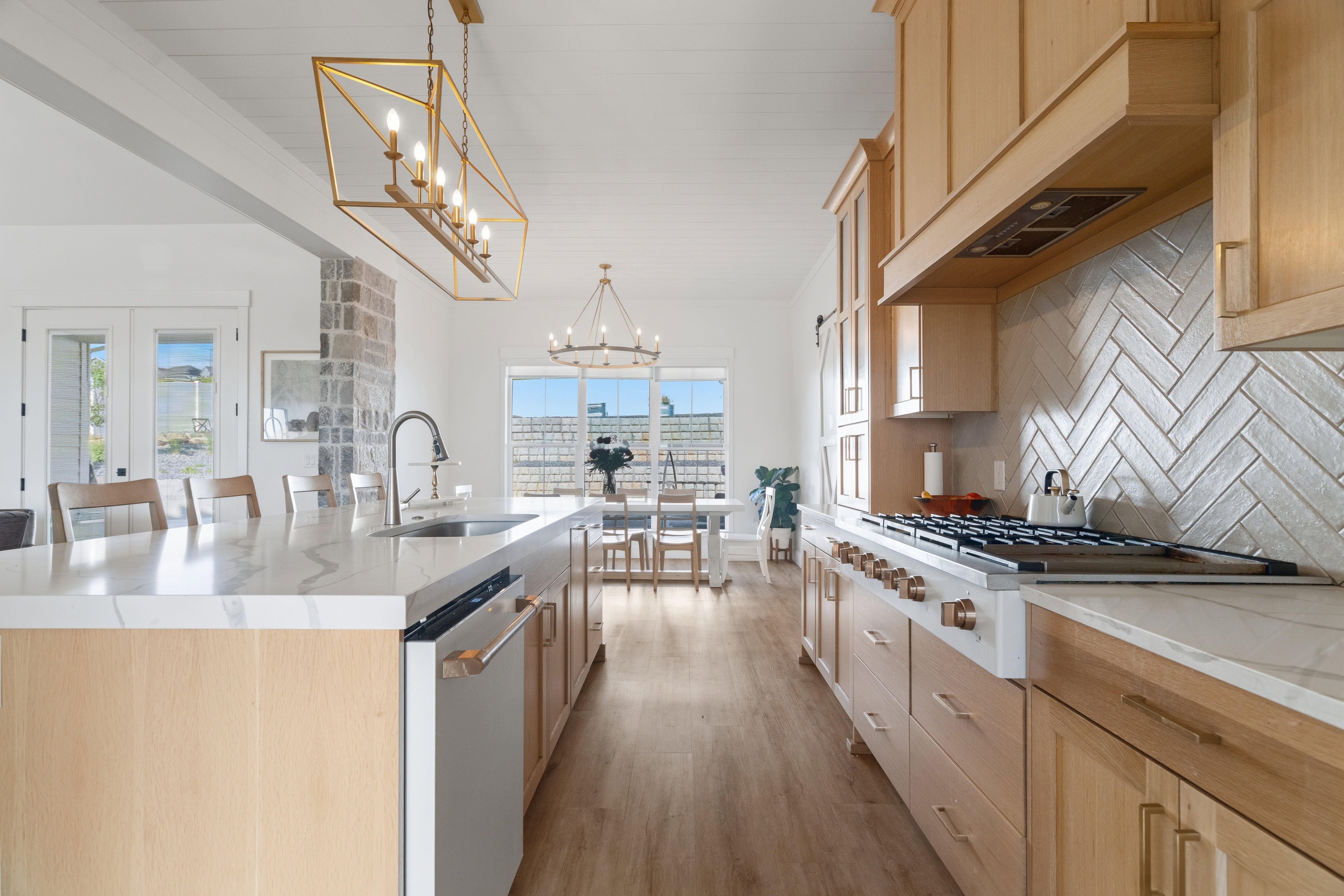 Open-concept kitchen featuring light wood cabinetry, white quartz countertops, a herringbone tile backsplash, and wood-finish flooring