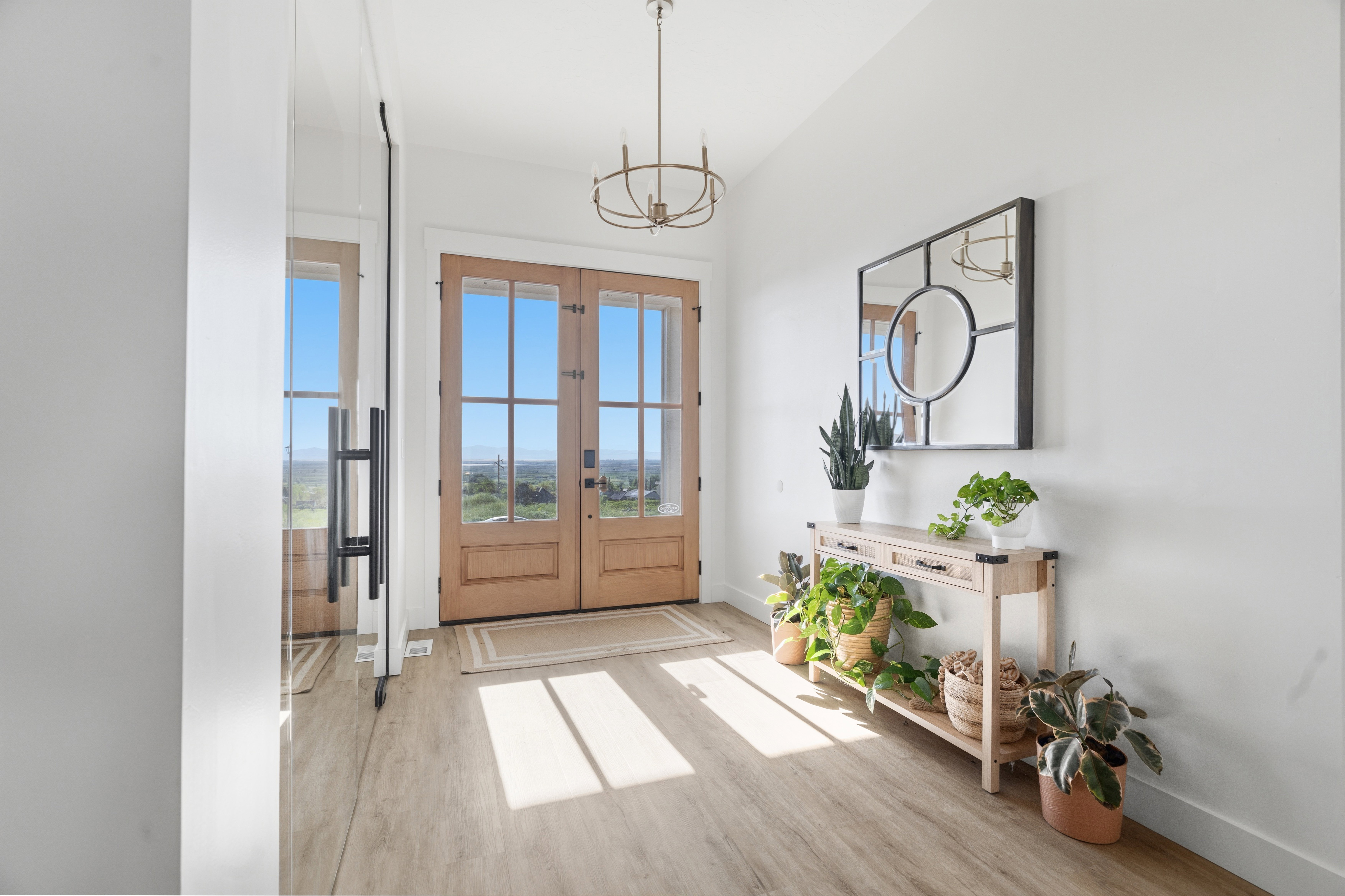 Entryway featuring light wood-finish flooring, a contemporary chandelier, double glass-paneled entry doors, and a large wall-mounted mirror