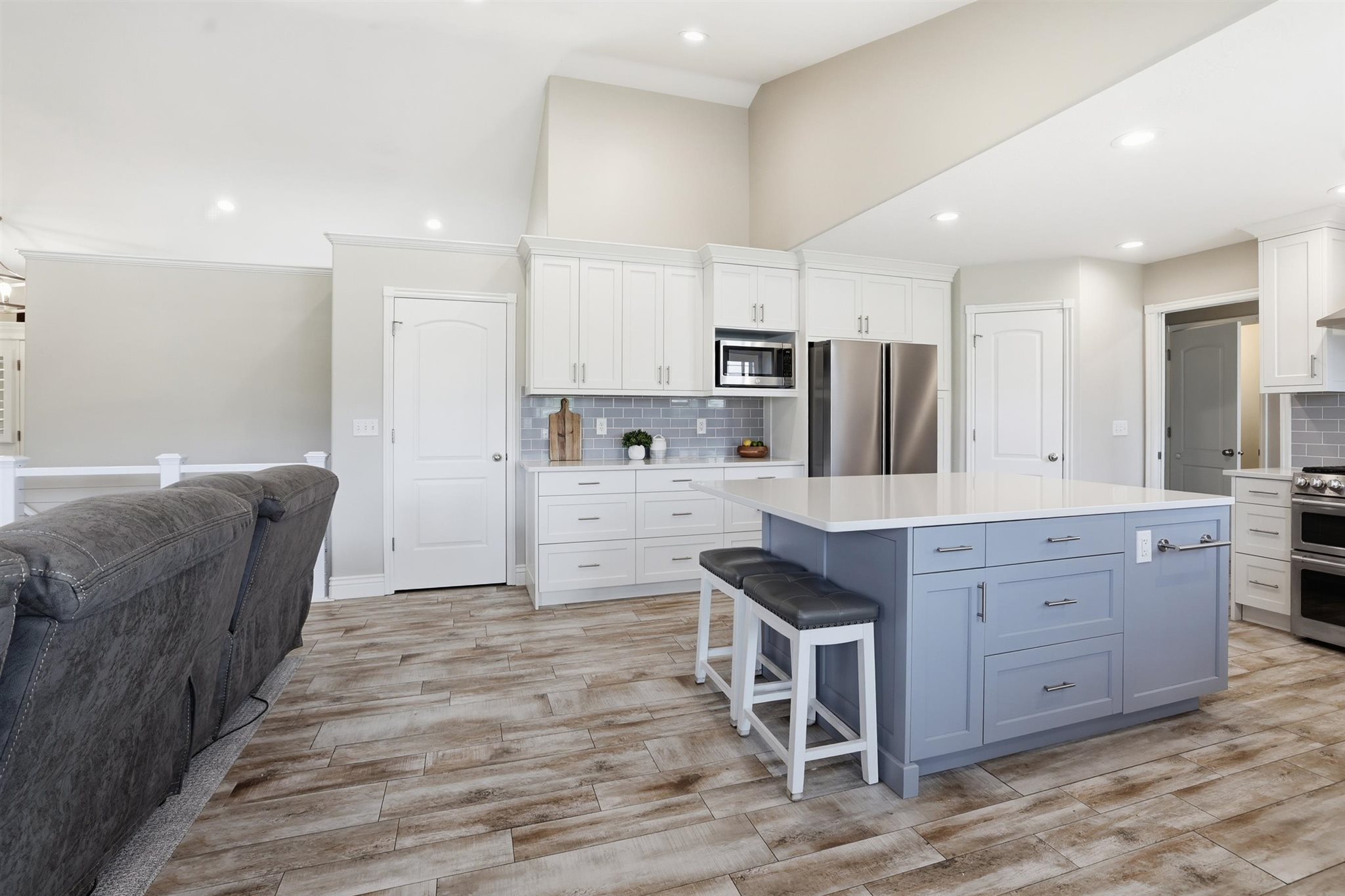 Spacious kitchen featuring a large island with light blue cabinetry, white perimeter cabinetry, stainless steel appliances, and a gray subway tile backsplash