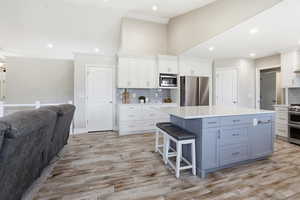 Spacious kitchen featuring a large island with light blue cabinetry, white perimeter cabinetry, stainless steel appliances, and a gray subway tile backsplash