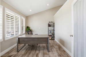 Room featuring wood-finish flooring, multiple windows with white plantation shutters, an angled ceiling, recessed lighting, and a white interior door
