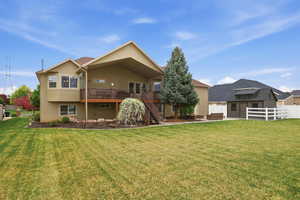 Spacious backyard featuring a large green lawn, a multi-level deck with stairs, mature landscaping, and a detached shed with a white picket fence