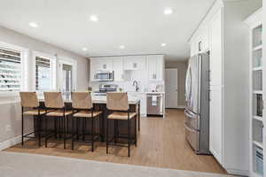 Modern kitchen featuring white cabinetry, stainless steel appliances, a center island with seating, wood-finish flooring, and recessed lighting
