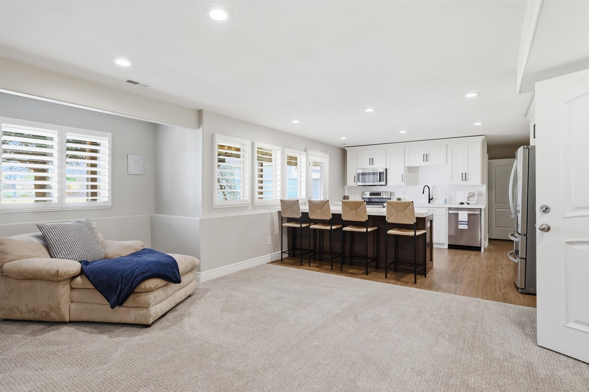 Open-concept living space featuring recessed lighting, a modern kitchen island with seating, stainless steel appliances, and white plantation shutters