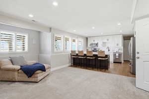Open-concept living space featuring recessed lighting, a modern kitchen island with seating, stainless steel appliances, and white plantation shutters