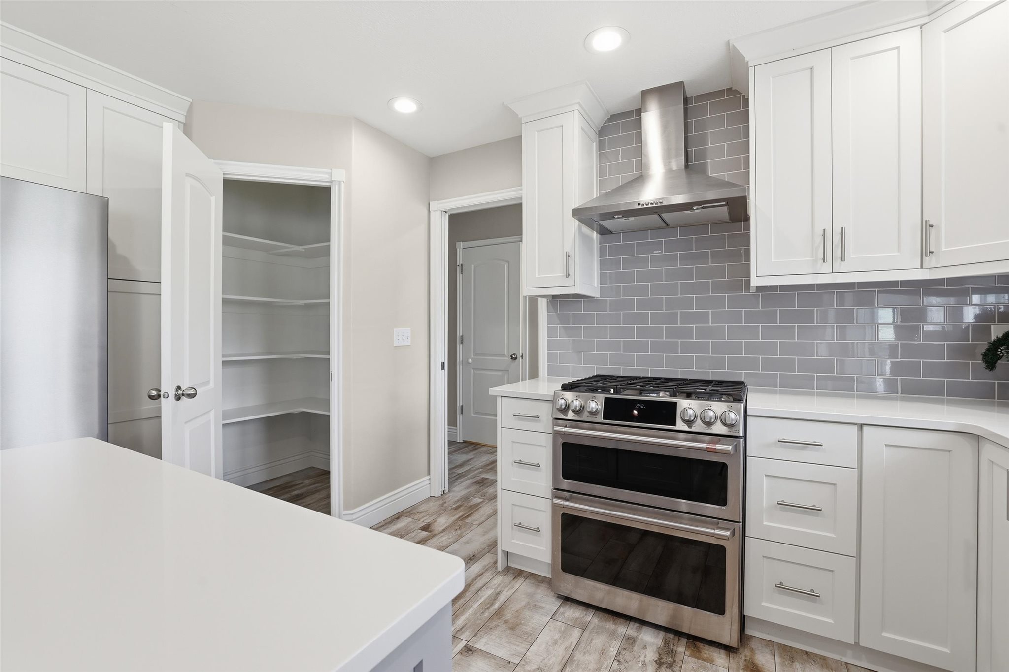 Modern kitchen featuring white cabinetry, light countertops, a stainless steel range with a double oven, a stainless steel range hood, and a gray subway tile backsplash