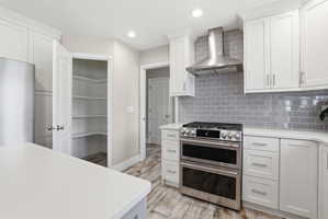 Modern kitchen featuring white cabinetry, light countertops, a stainless steel range with a double oven, a stainless steel range hood, and a gray subway tile backsplash