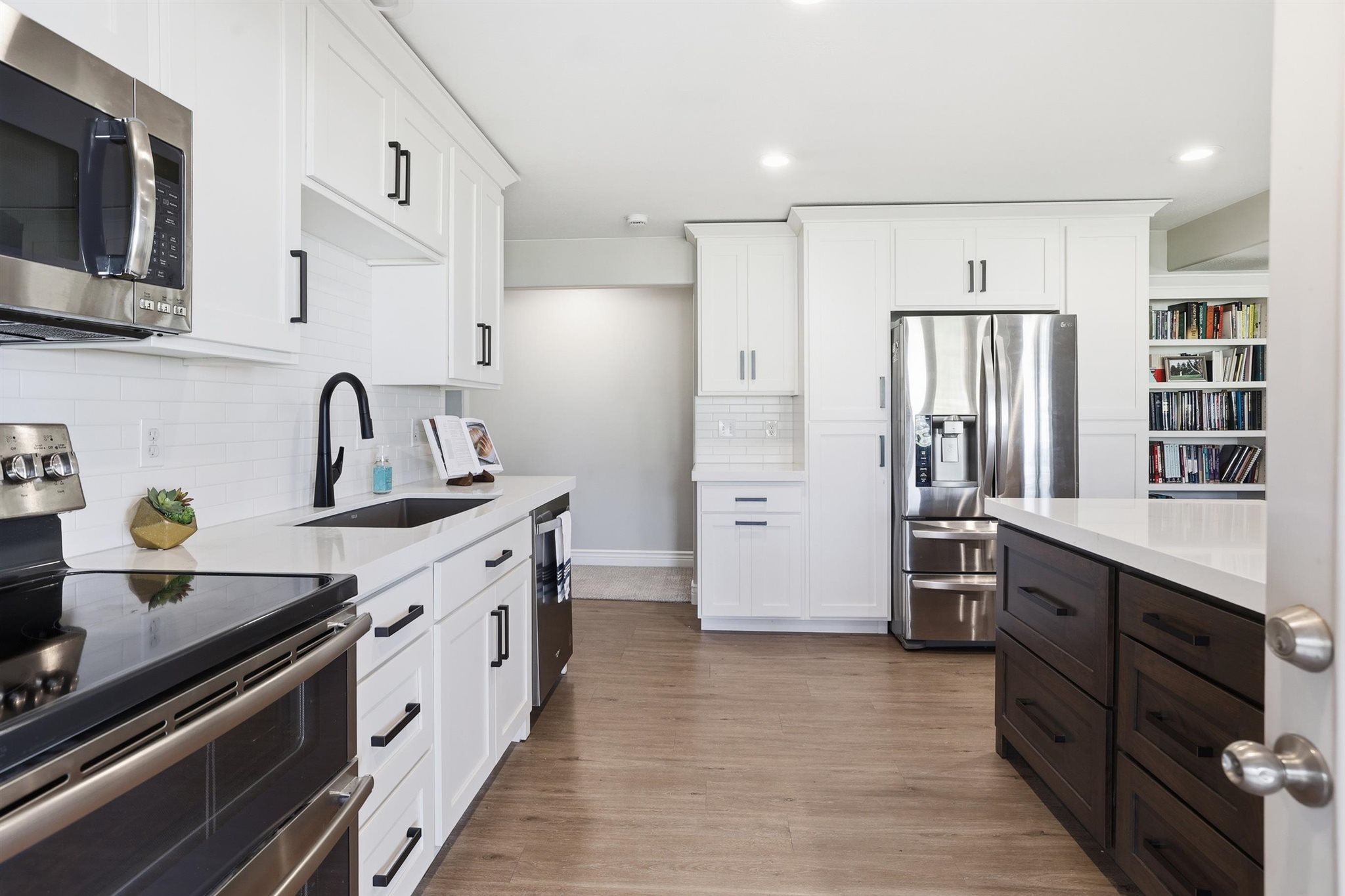 Modern kitchen featuring white cabinetry, stainless steel appliances, a large center island with dark wood-finish cabinetry, and wood-finish flooring