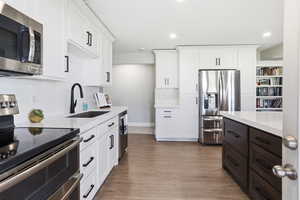 Modern kitchen featuring white cabinetry, stainless steel appliances, a large center island with dark wood-finish cabinetry, and wood-finish flooring