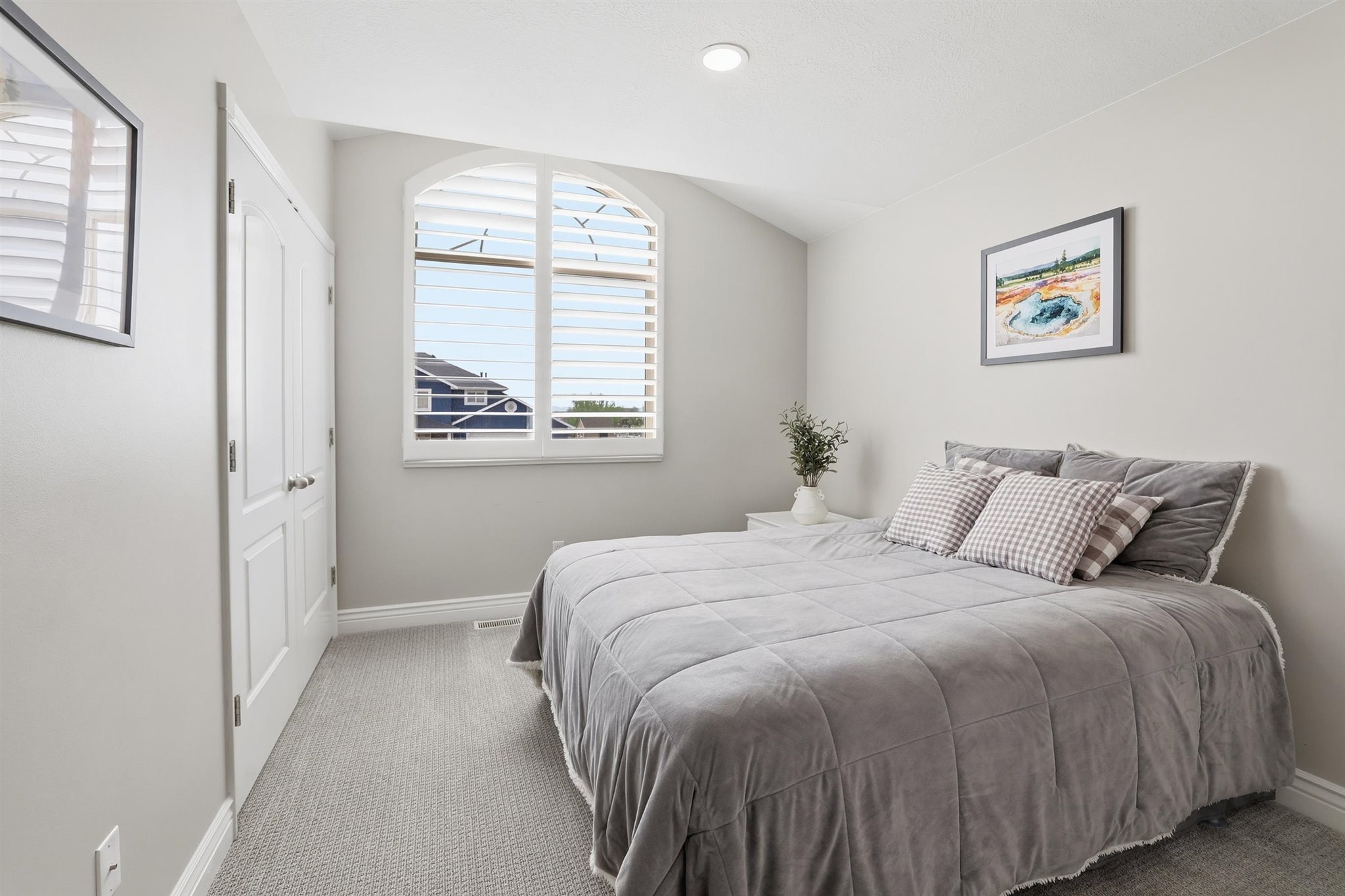 Arch-top window with white plantation shutters, neutral gray walls, light gray carpeting, and a double-door closet