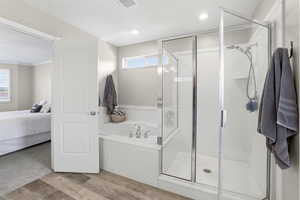 Bathroom featuring a glass-enclosed standing shower, a built-in tub with chrome fixtures, and wood-finish flooring