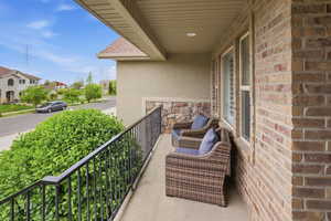 Covered balcony featuring brick and stone veneer siding, stucco accents, and a black wrought iron railing