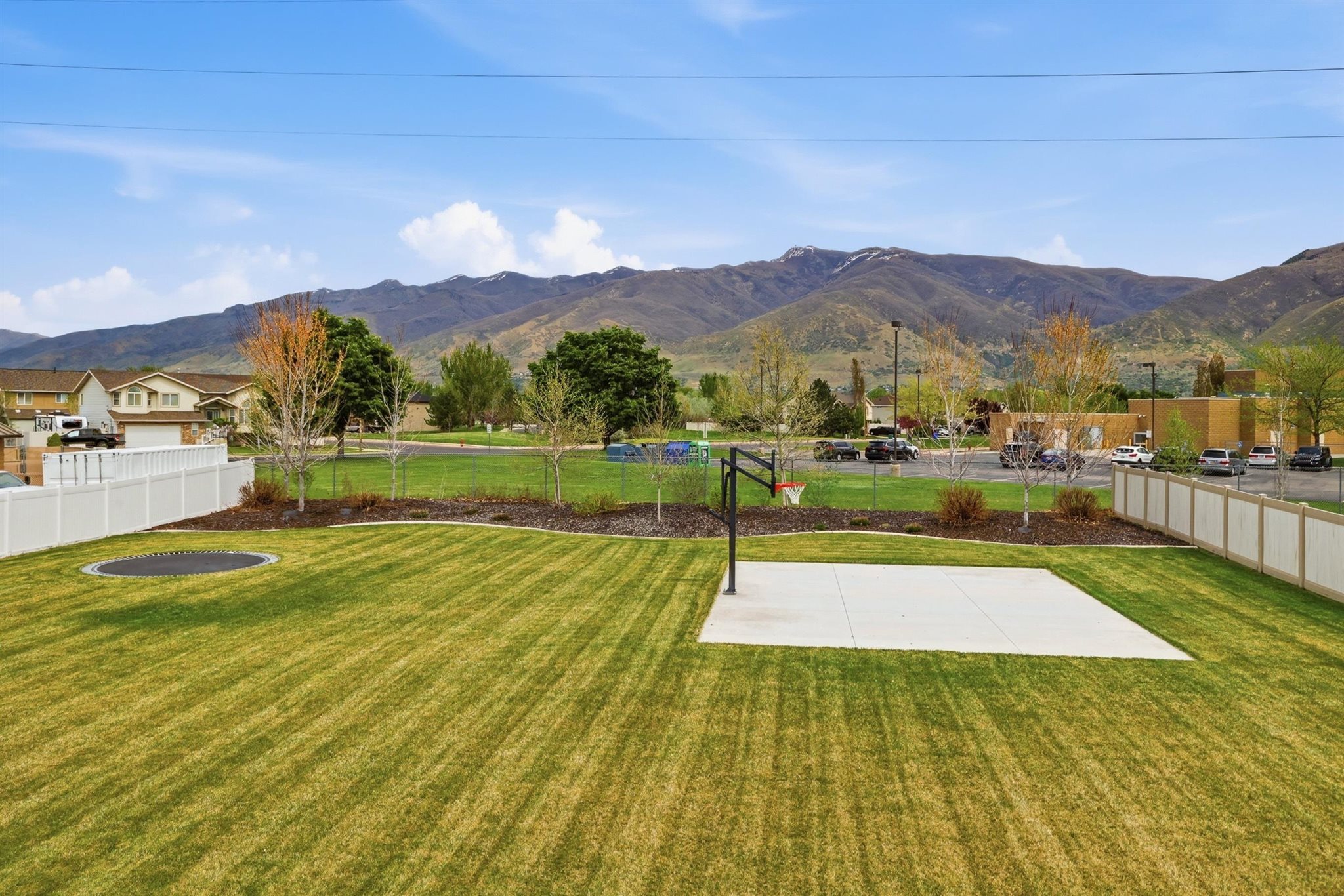 Expansive green lawn with a visible concrete sports court and an in-ground trampoline