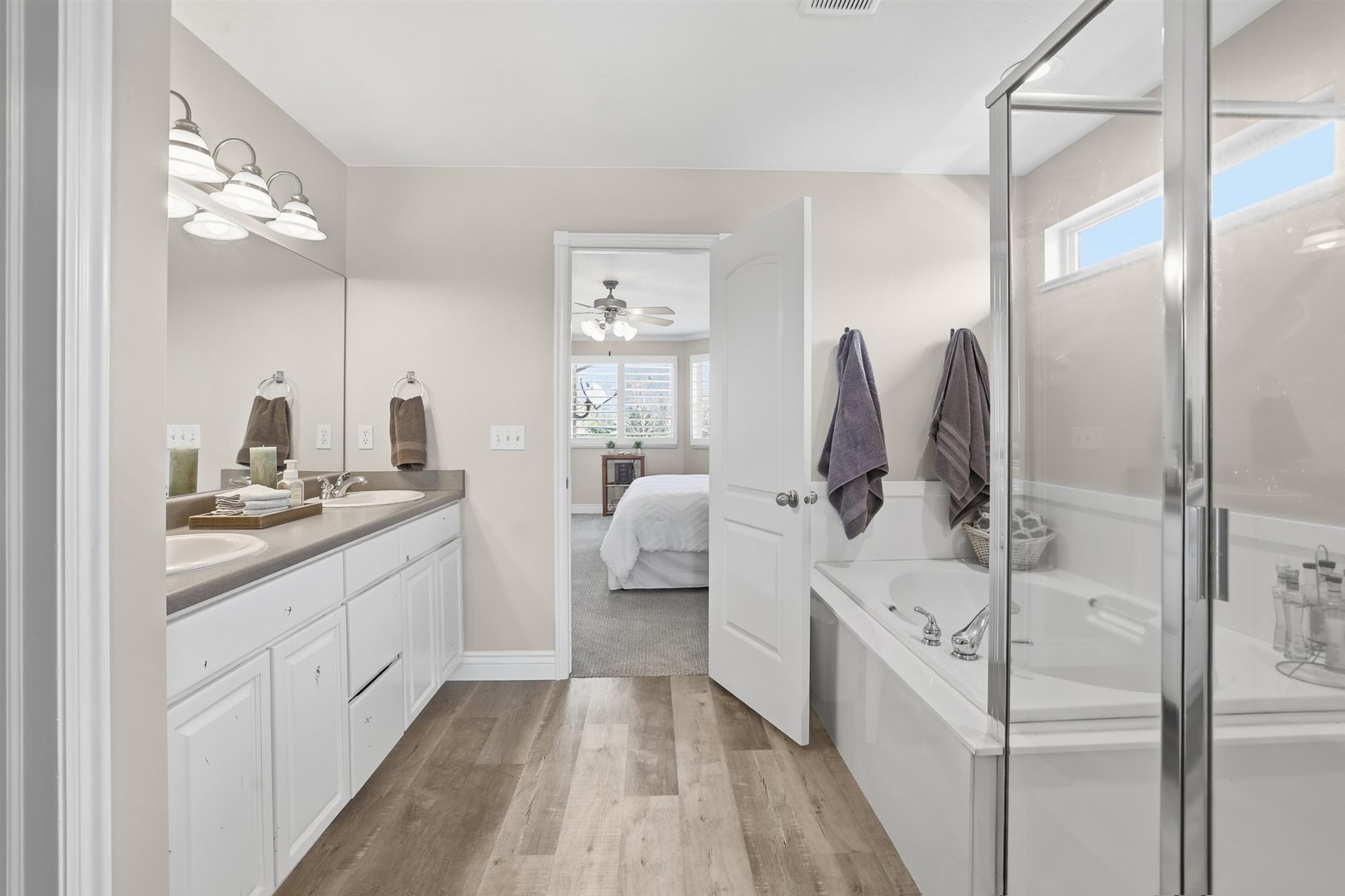 Bathroom featuring wood-finish flooring, a dual vanity with undermount sinks, and a built-in tub with an enclosed shower
