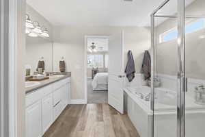 Bathroom featuring wood-finish flooring, a dual vanity with undermount sinks, and a built-in tub with an enclosed shower
