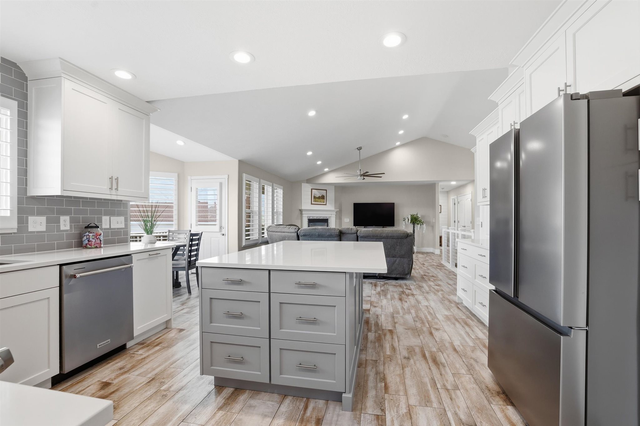 Open-concept kitchen featuring wood-finish flooring, a central island with gray cabinetry, white perimeter cabinetry, stainless steel appliances, and recessed lighting