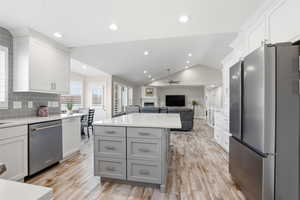 Open-concept kitchen featuring wood-finish flooring, a central island with gray cabinetry, white perimeter cabinetry, stainless steel appliances, and recessed lighting