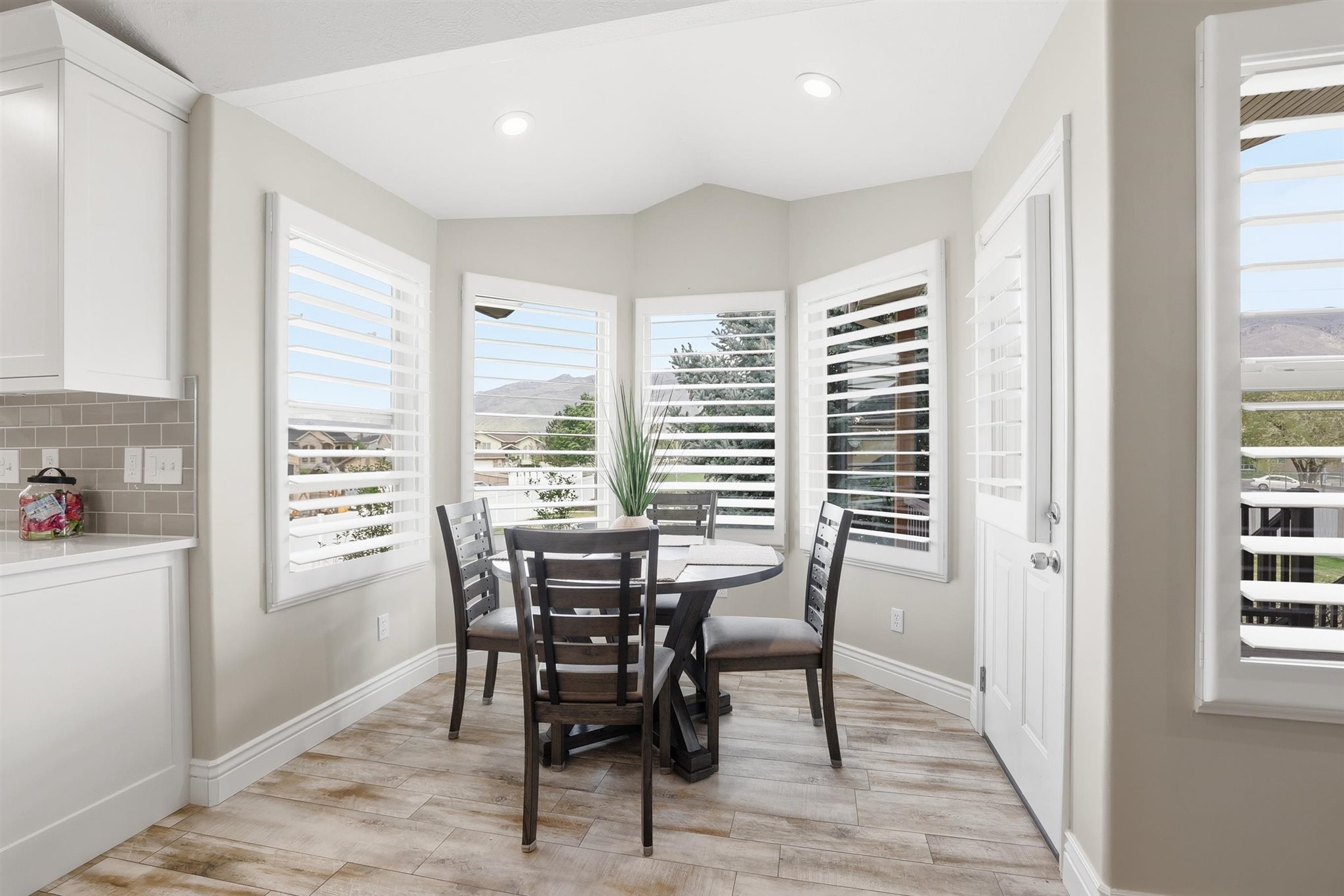 Bright dining nook featuring a bay window with plantation shutters, wood-finish flooring, recessed lighting, and a neutral color palette