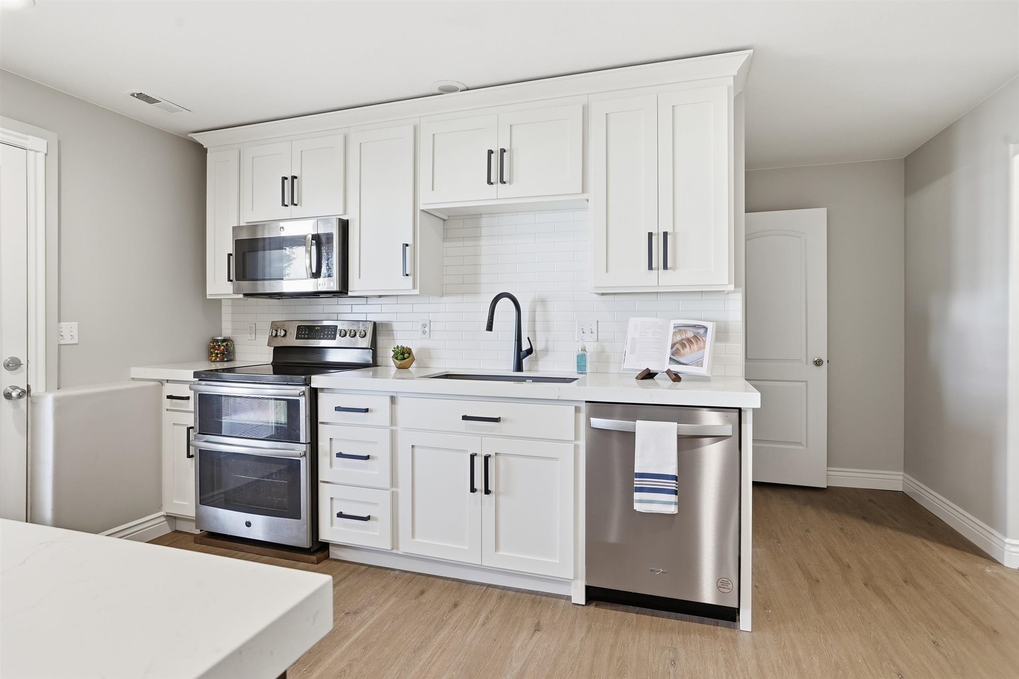 Contemporary kitchen featuring white cabinetry, stainless steel appliances, a subway tile backsplash, solid surface countertops, and wood-finish flooring